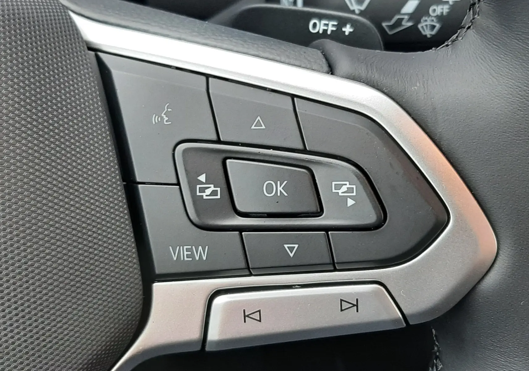 Gros plan sur les commandes multifonctions à gauche du volant cuir noir du Volkswagen T-Roc gris Pyrite 2025.