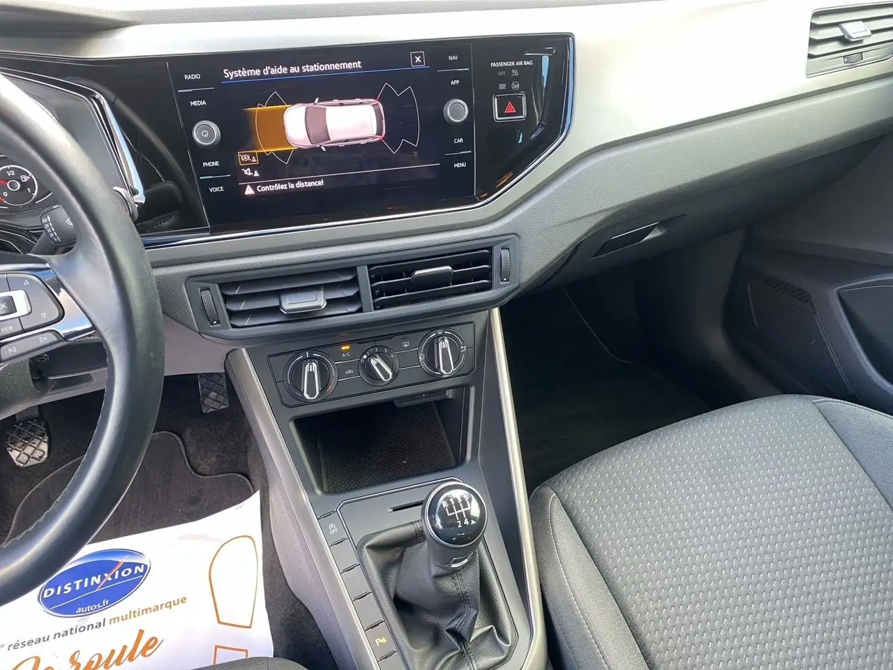 Vue intérieure côté conducteur de la Volkswagen Polo blanche, avec tableau de bord et levier de vitesses manuel en évidence.