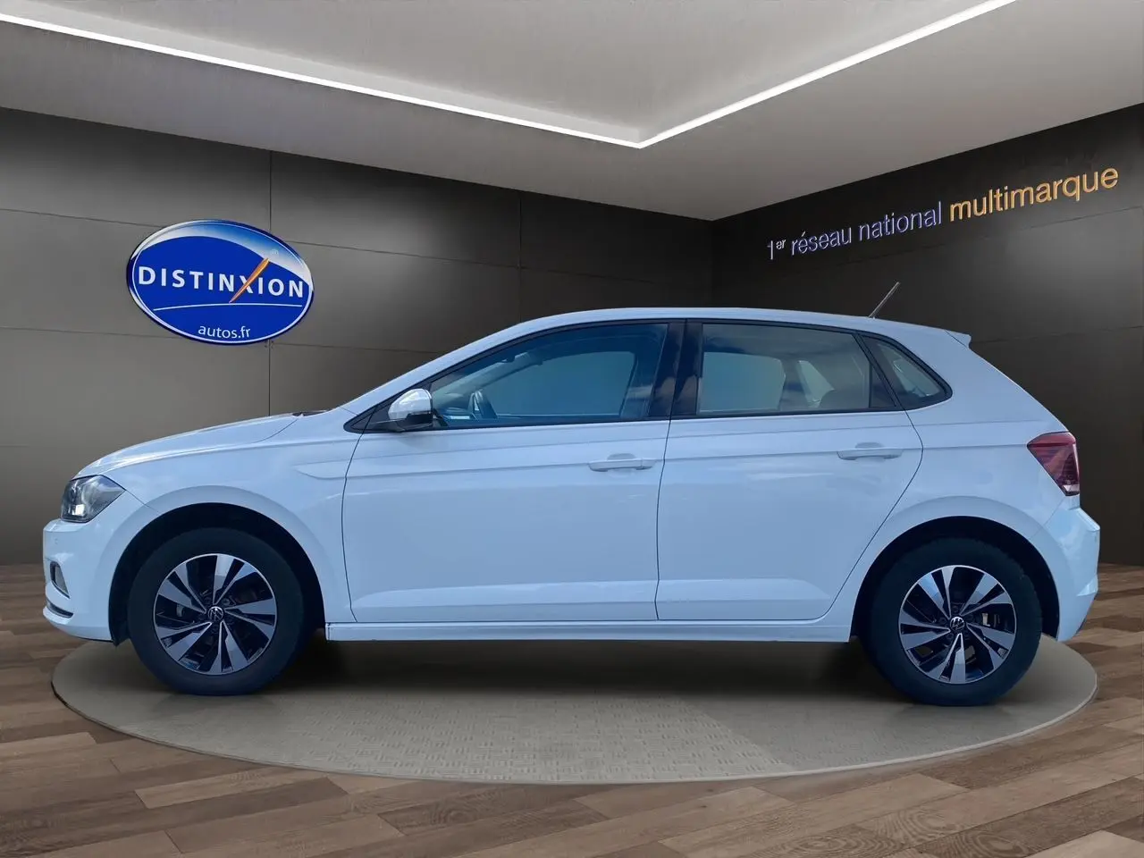 Volkswagen Polo blanc pure vue de profil côté gauche, avec jantes alliage et cinq portes visibles en intérieur showroom.