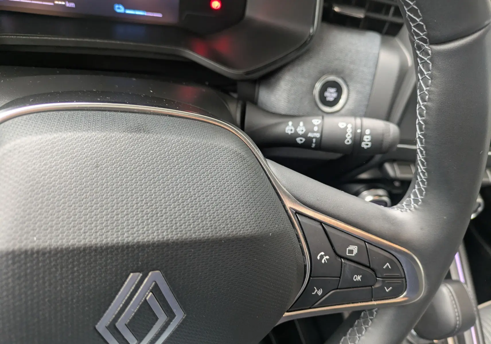 Gros plan sur le volant noir de la Renault Clio 2025, avec commandes multifonctions et bouton start/stop visible en arrière-plan.