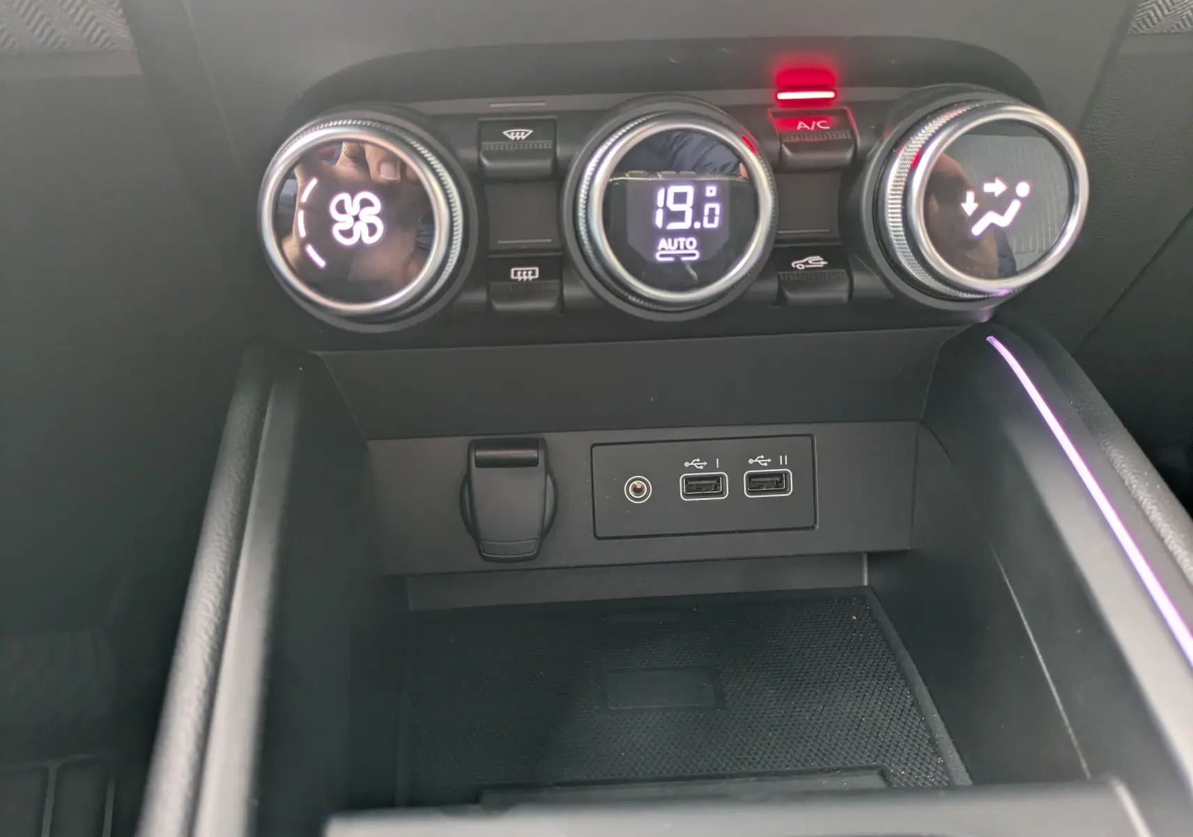 Vue rapprochée du tableau de bord de la Renault Clio 2025, montrant les commandes de climatisation et ports USB sur fond noir.