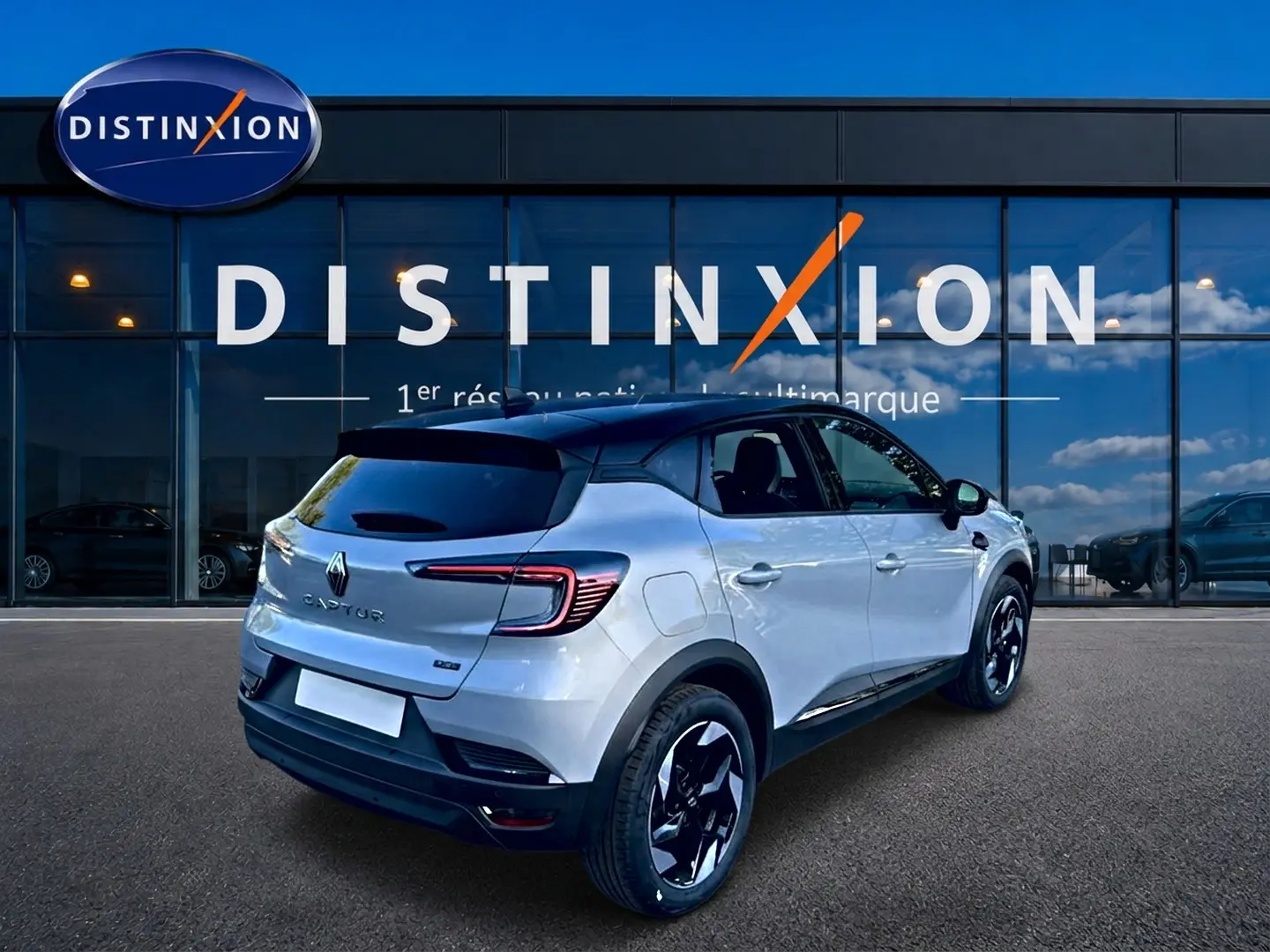 Vue 3/4 arrière droite du Renault Captur gris rafale avec toit noir et jantes alu noires devant une vitrine Distinxion.