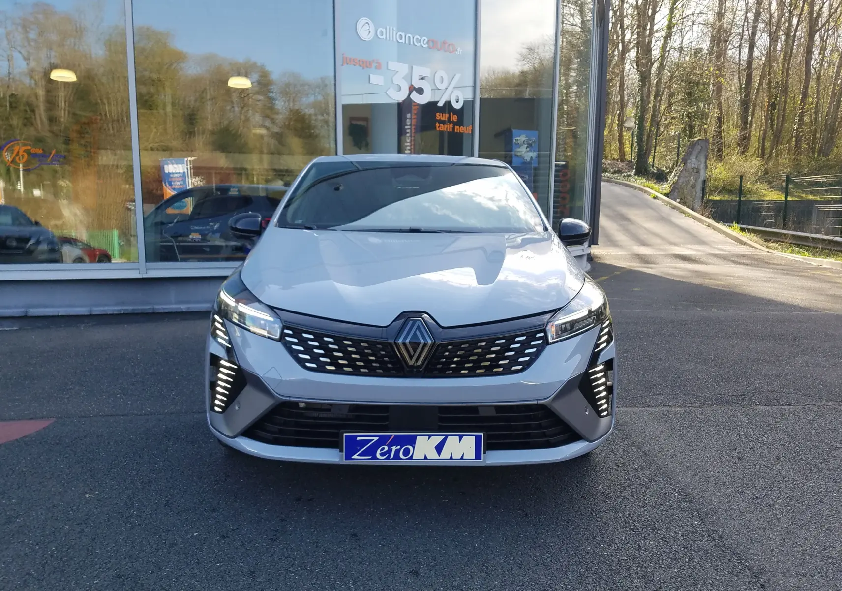 Vue de face d'une Renault Clio V gris rafale avec feux LED allumés et calandre noire à motifs argentés.