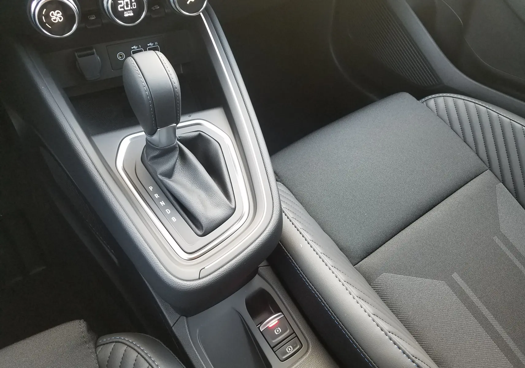 Gros plan sur la console centrale et le levier de vitesse automatique de la Renault Clio V gris Rafale, avec accoudoir noir et coutures bleues.