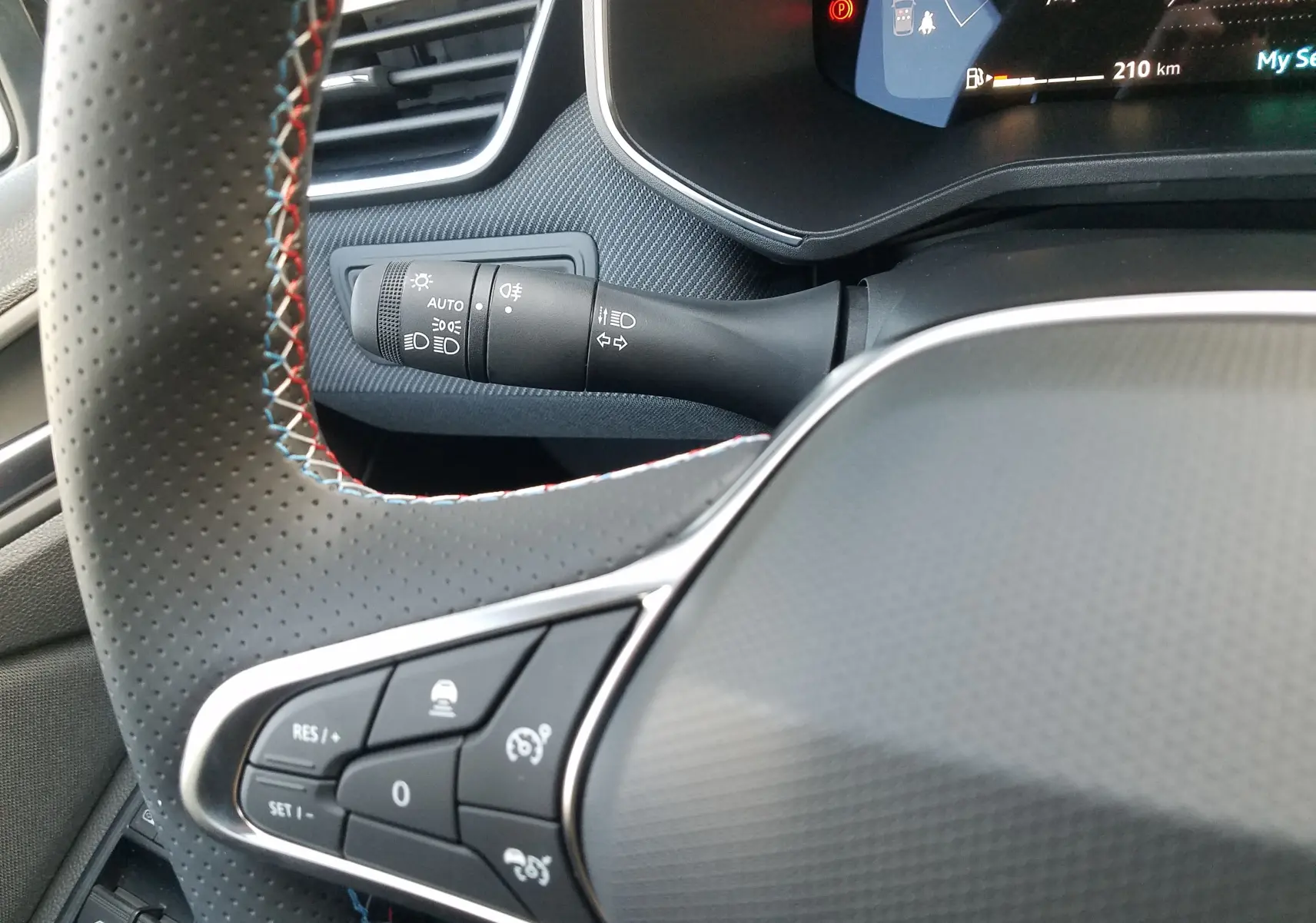 Gros plan sur le volant perforé avec surpiqûres tricolores et commandes intégrées de la Renault Clio V hybride 2025.