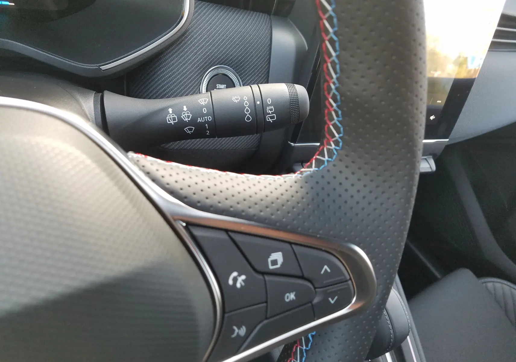 Détail du volant perforé avec surpiqûres tricolores et commandes intégrées dans l'habitacle de la Renault Clio V hybride.