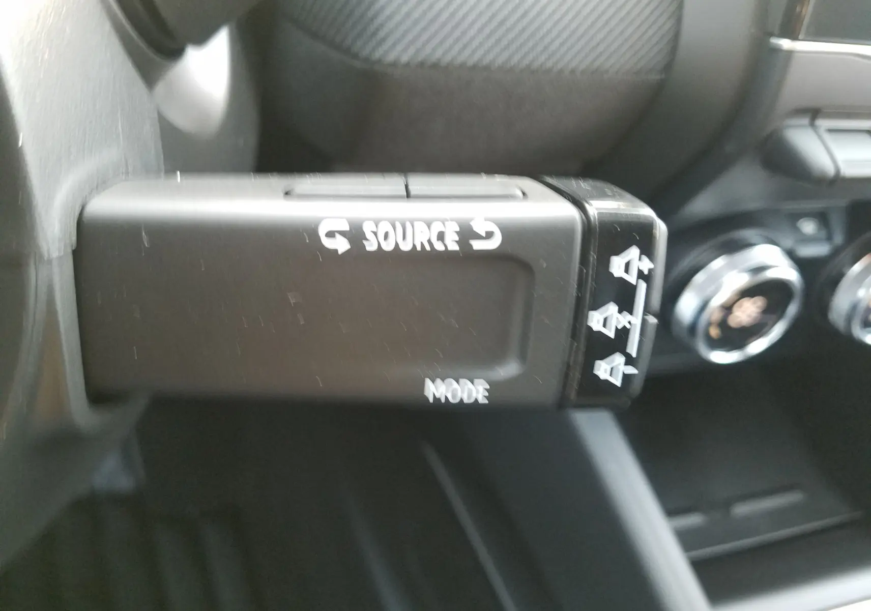 Gros plan sur la commande au volant de la Renault Clio V hybride 2025, boutons source et mode visibles en noir.