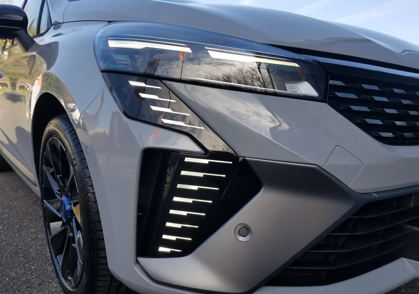 Gros plan sur l'avant gauche de la Renault Clio V gris Rafale, mettant en valeur ses phares LED et jante noire sportive.