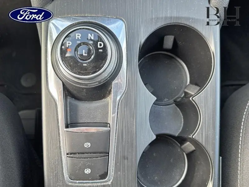 Vue rapprochée de la console centrale gris foncé du Ford Kuga 2022 avec sélecteur rotatif de boîte auto et porte-gobelets.