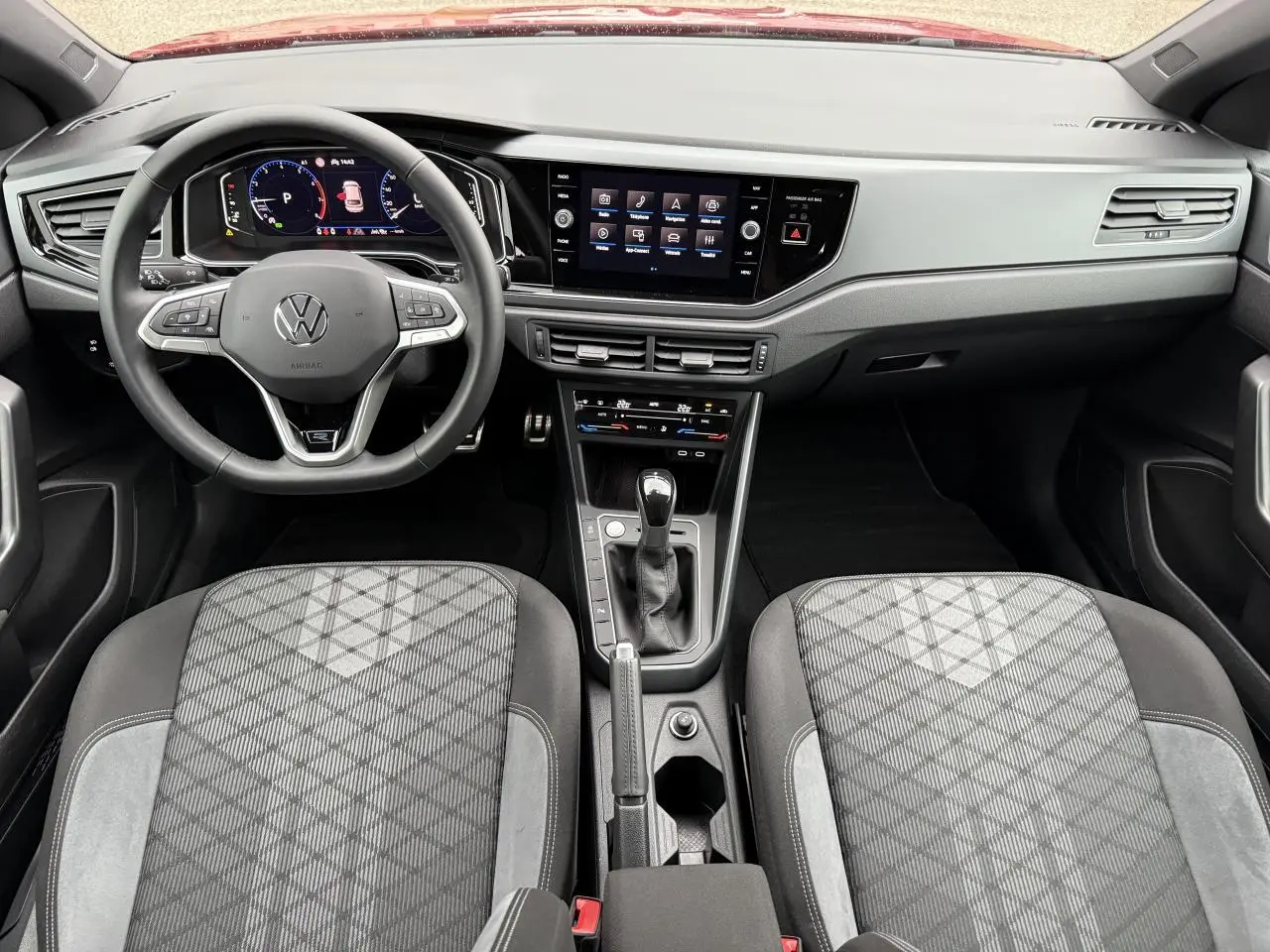 Vue intérieure avant du Volkswagen Taigo 2025, tableau de bord moderne avec écran tactile et sièges tissu gris à motifs géométriques.