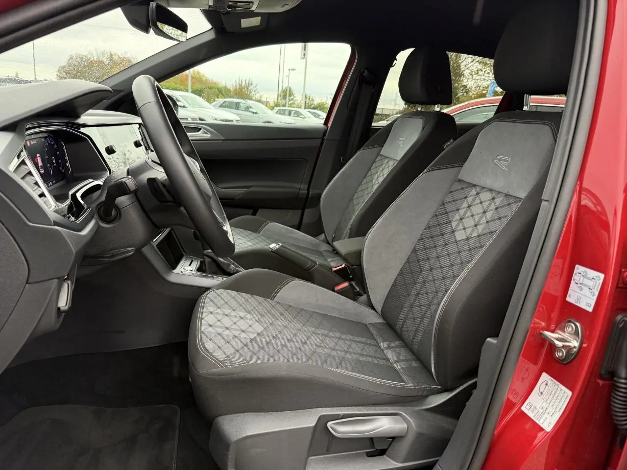 Vue intérieure côté gauche du Volkswagen Taigo Rouge Roi 2025, sièges Sport-Confort gris avec logo R brodé.