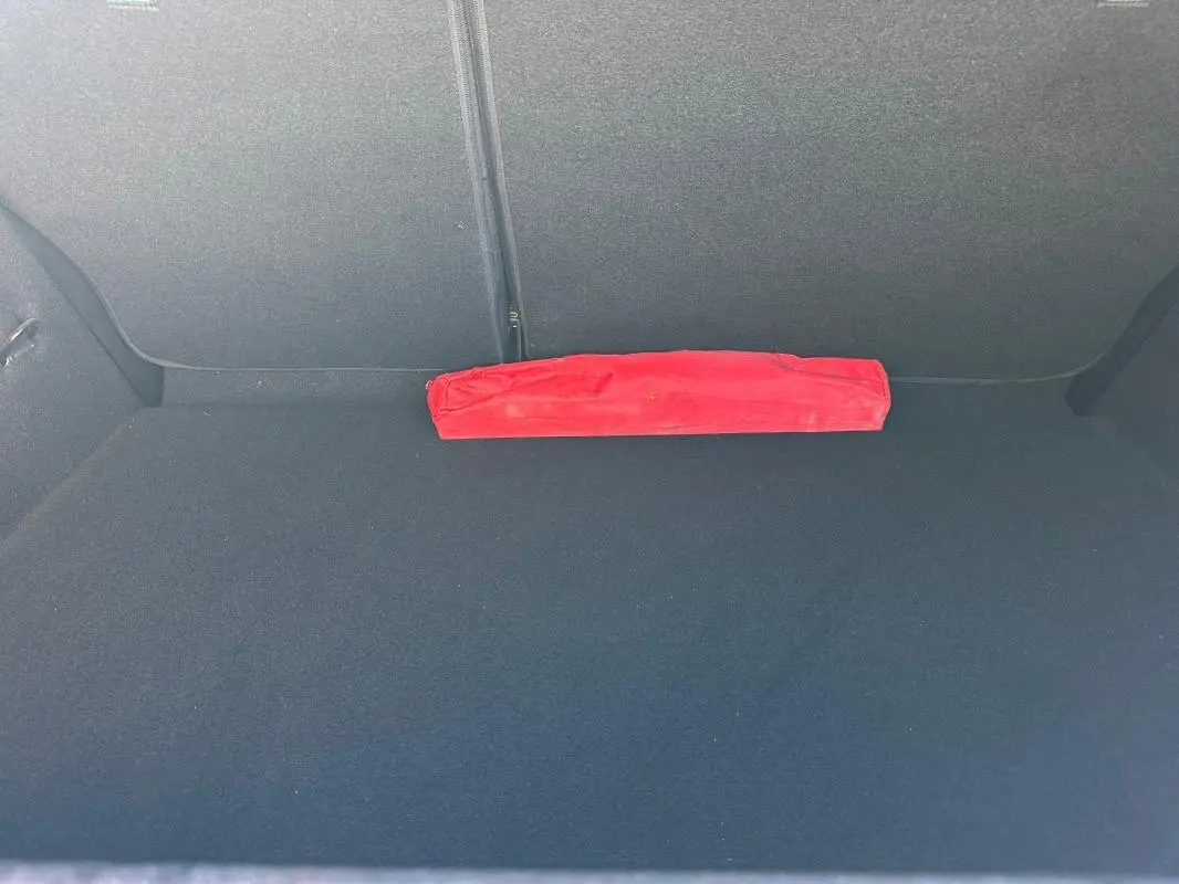 Coffre vide d'une Renault Clio bleu foncé 2023, avec un triangle de signalisation rouge posé à plat.