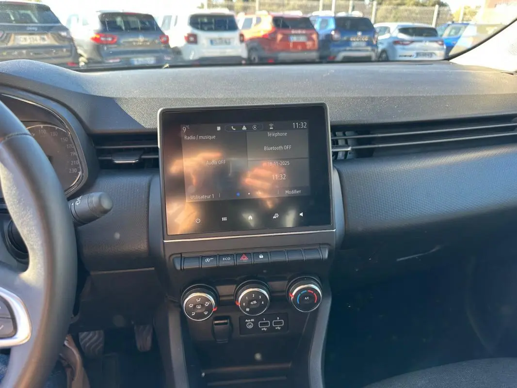 Vue intérieure du tableau de bord de la Renault Clio bleu foncé 2023, avec écran tactile central et commandes de climatisation manuelle.