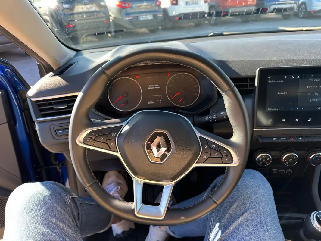 Vue intérieure centrée sur le volant de la Renault Clio bleu foncé 2023, avec tableau de bord et écran tactile visibles.