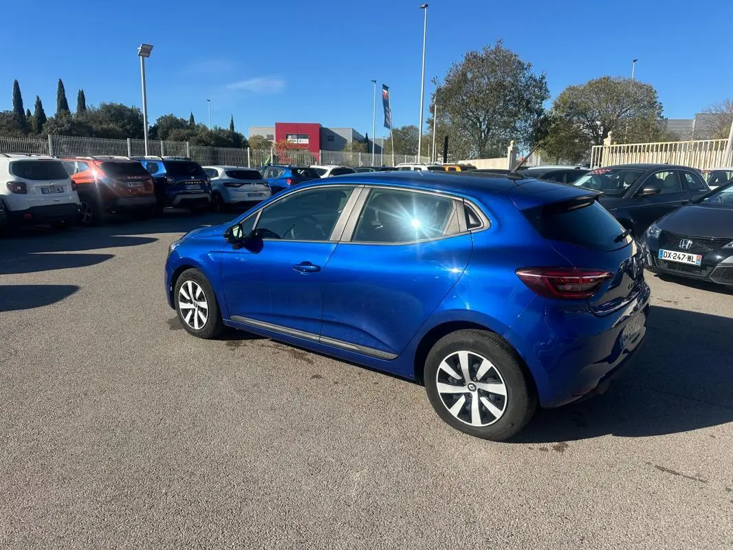 Renault Clio V TCe 90 bleu foncé vue de trois quarts arrière droit sur parking ensoleillé.