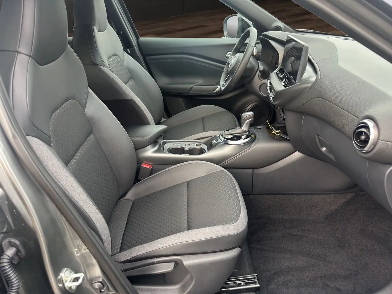 Vue intérieure côté conducteur du Nissan Juke 1.6 Hybrid 2025 gris squale, avec sièges et volant chauffants visibles.