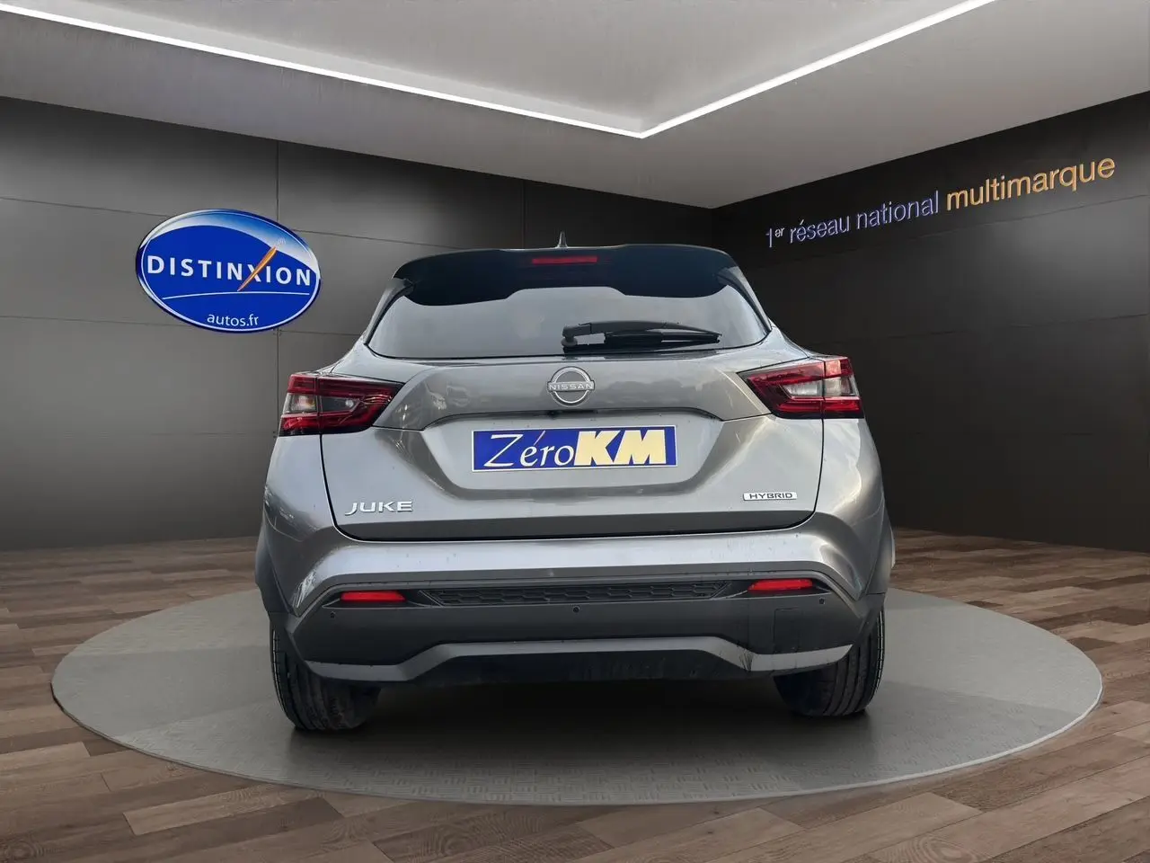 Vue arrière d'un Nissan Juke 2025 gris squale hybride, avec feux arrière LED et logo distinctif sur un podium intérieur.