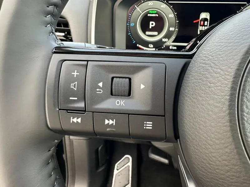 Gros plan sur les commandes au volant côté gauche du Nissan Qashqai Hybrid e-POWER 2025 avec tableau de bord numérique en arrière-plan.