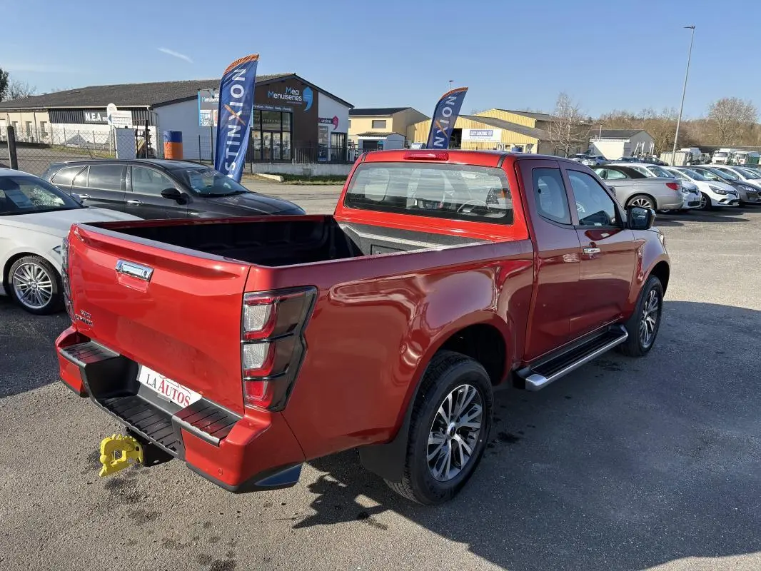 Vue 3/4 arrière droite d'un pick-up Isuzu D-MAX rouge avec benne ouverte et jantes aluminium sur parking.