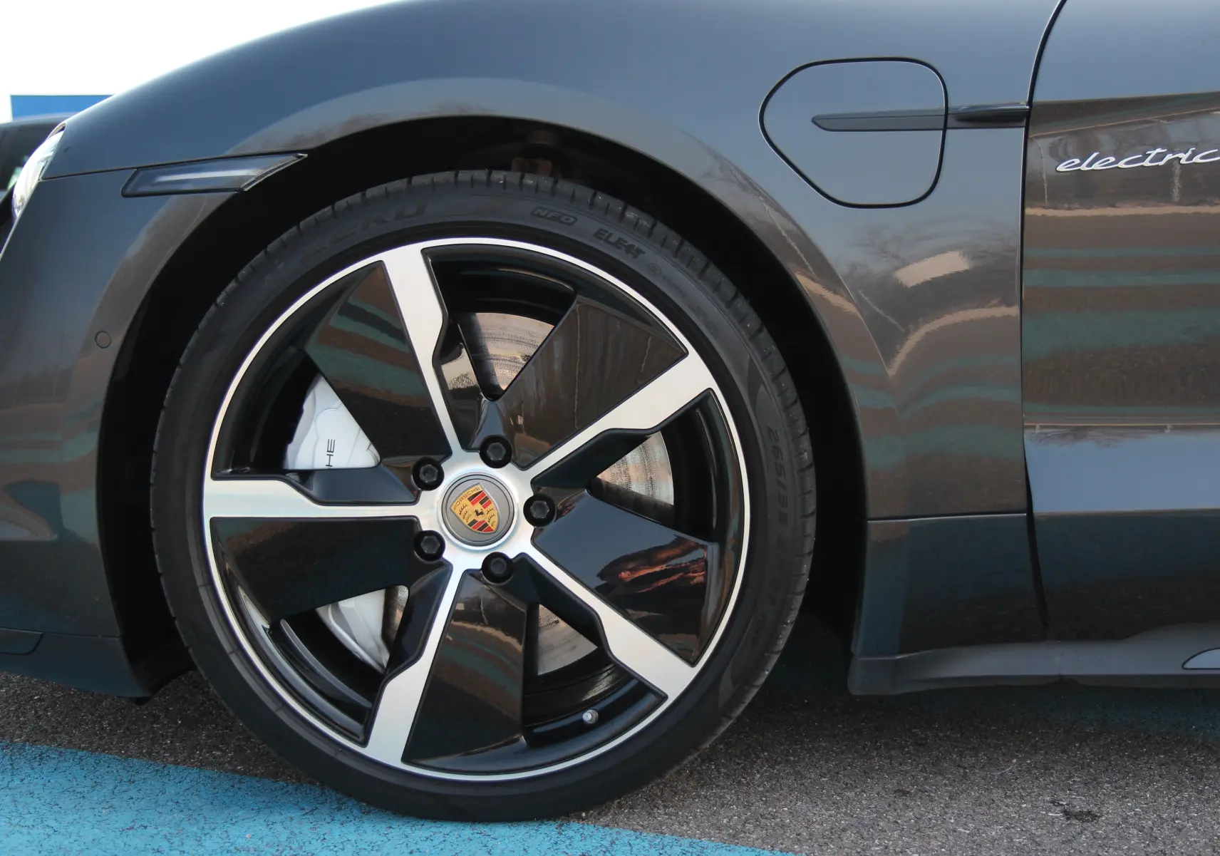 Gros plan sur la roue avant gauche d'une Porsche Taycan Turbo gris anthracite avec logo Porsche et inscription "electric" sur la portière.