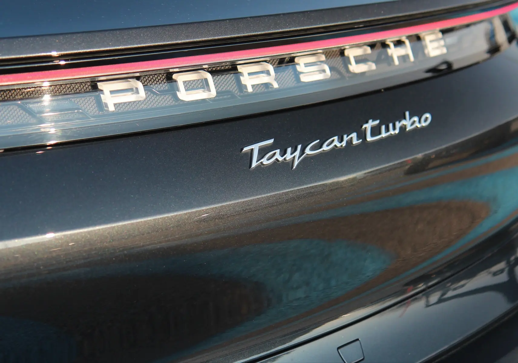 Gros plan sur l'arrière gris anthracite du Porsche Taycan Turbo avec logo et bande lumineuse rouge intégrée.