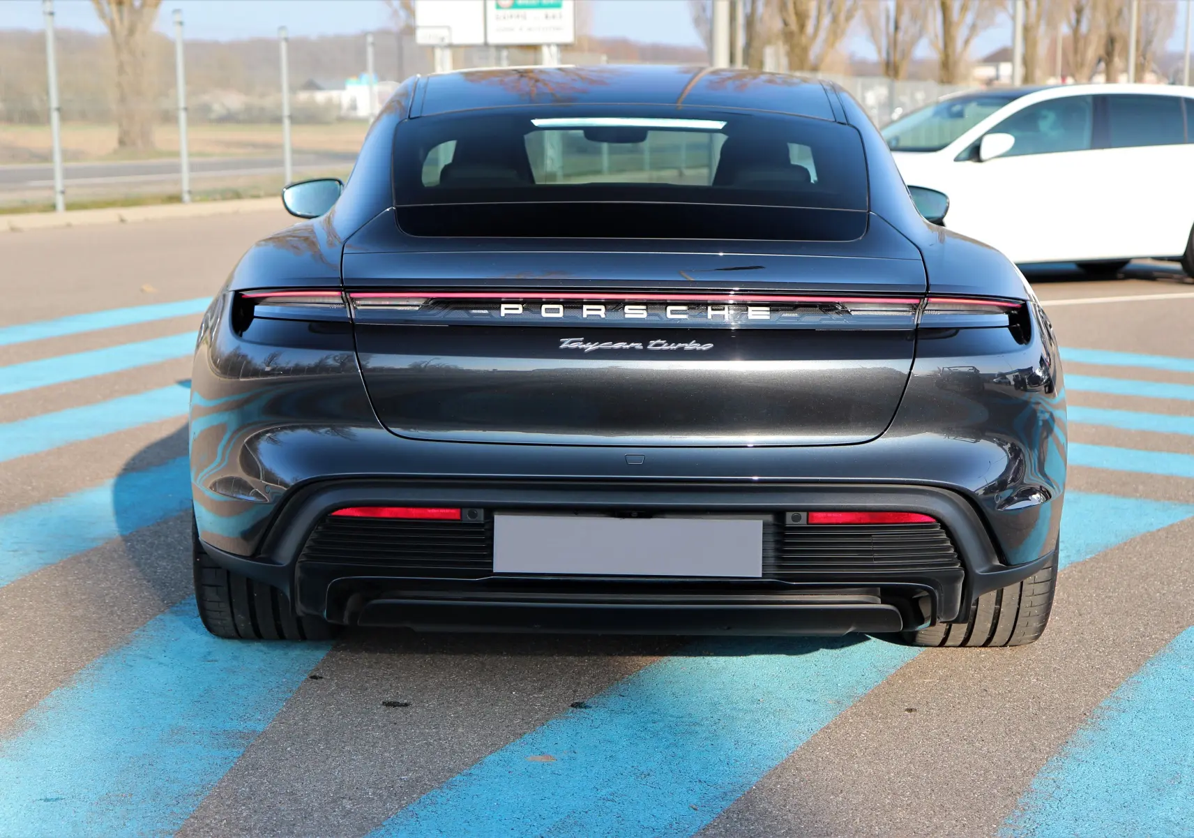 Vue arrière d'une Porsche Taycan Turbo gris anthracite avec signature lumineuse et logo distinctif Porsche.