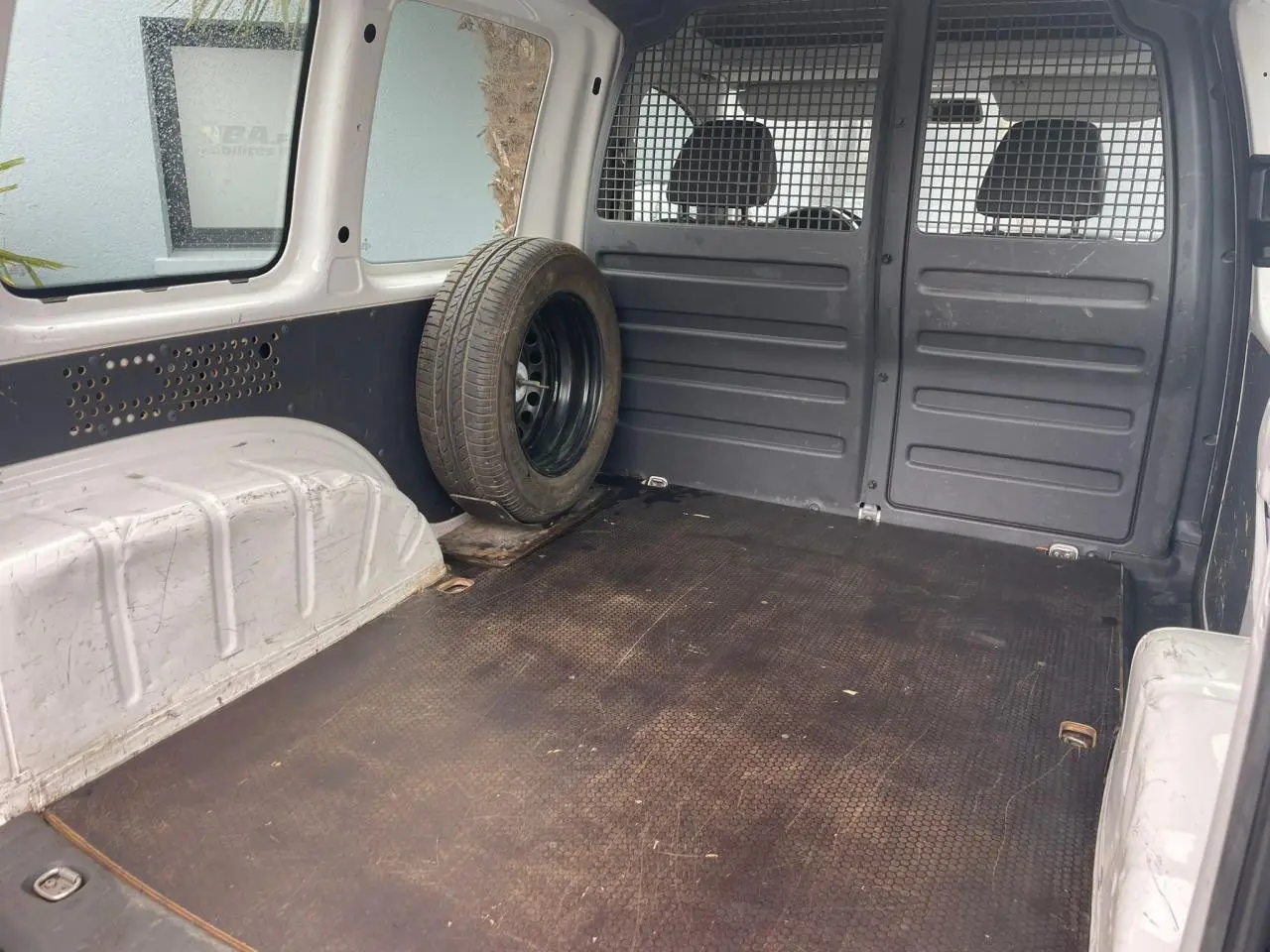 Vue intérieure arrière du Volkswagen Caddy blanc Candy 2014, montrant l'espace de chargement avec roue de secours fixée à gauche.