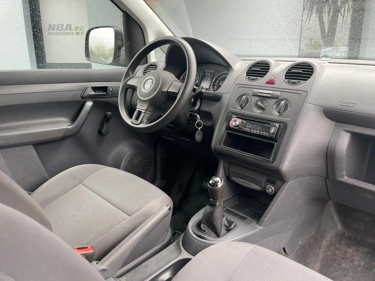 Intérieur du Volkswagen Caddy 2014 vu côté conducteur, tableau de bord gris avec boîte manuelle et volant noir.