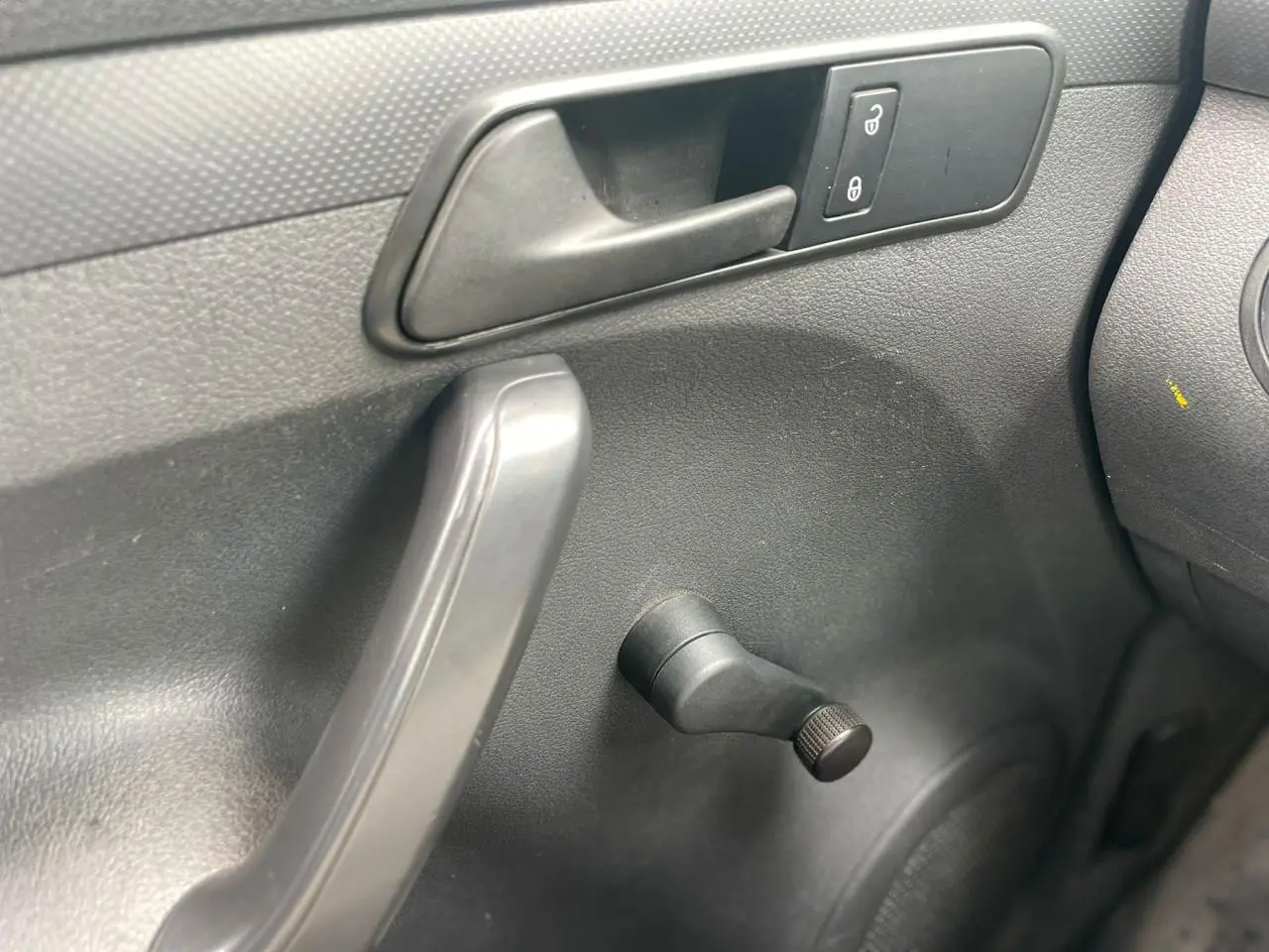 Détail de la manivelle de lève-vitre côté conducteur du Volkswagen Caddy blanc Candy 2014, intérieur noir.