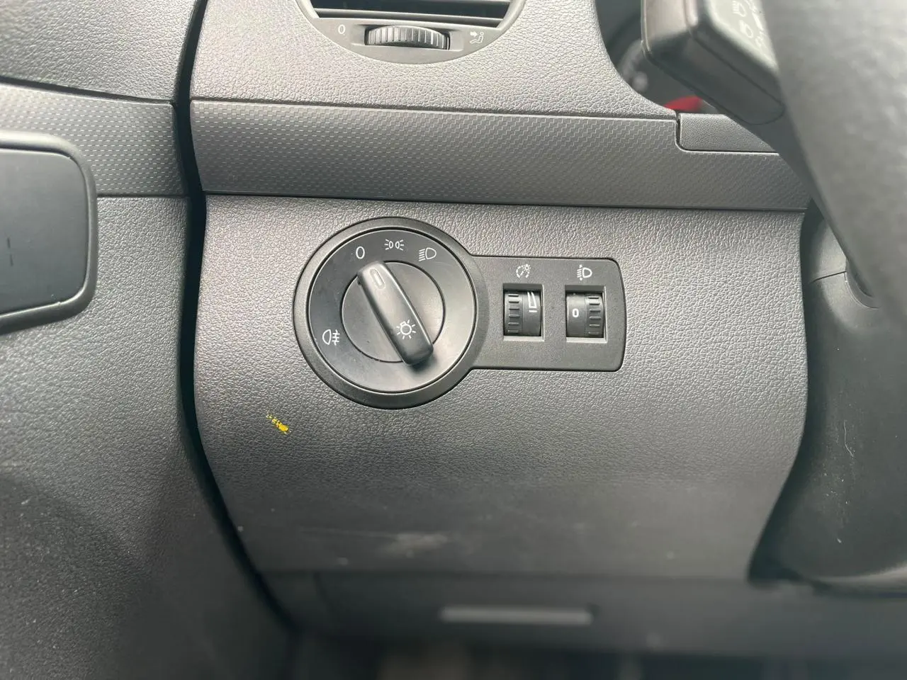 Gros plan sur le bouton de réglage des phares dans l'habitacle du Volkswagen Caddy blanc Candy de 2014.