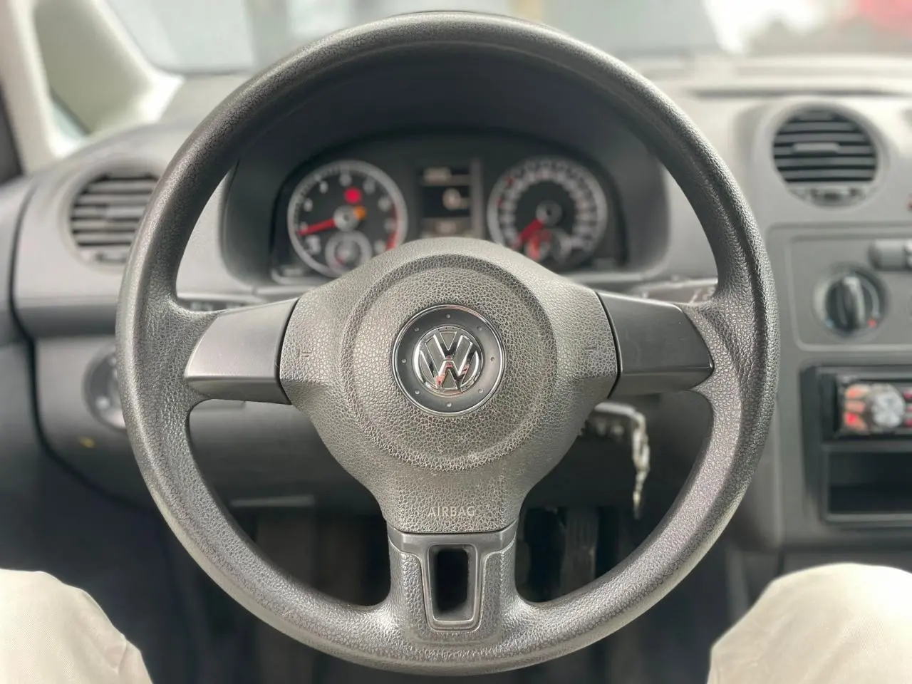 Vue rapprochée du volant noir de la Volkswagen Caddy 2014 avec tableau de bord et commandes visibles en arrière-plan.