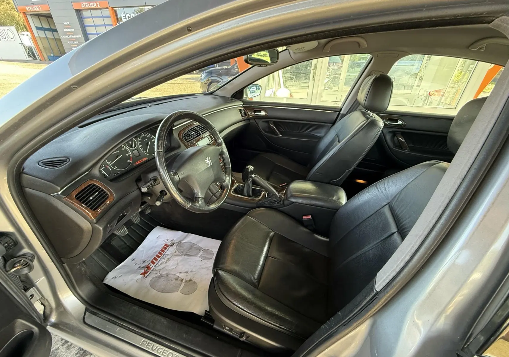 Intérieur d'une Peugeot 607 gris, vue côté conducteur, sièges cuir noir et tableau de bord avec bois.
