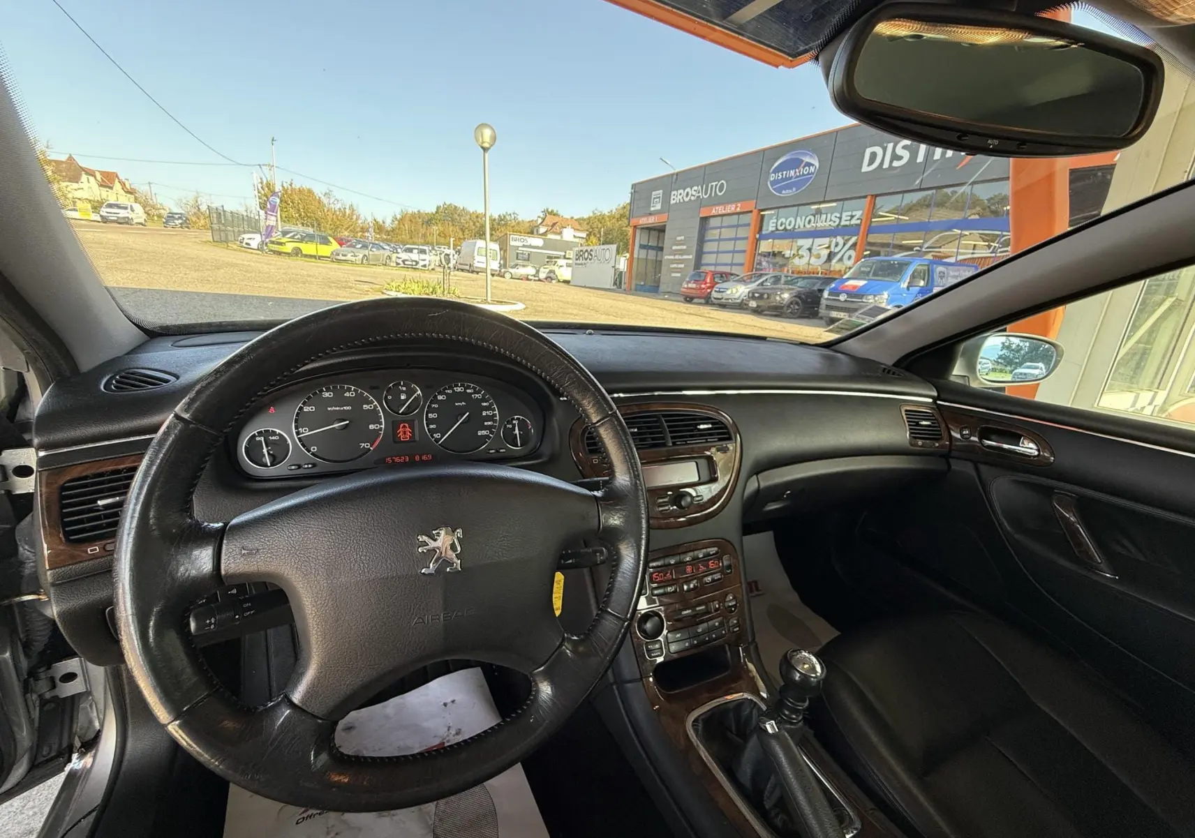 Vue intérieure du poste de conduite d'une Peugeot 607 gris, volant cuir et tableau de bord avec commandes boisées.
