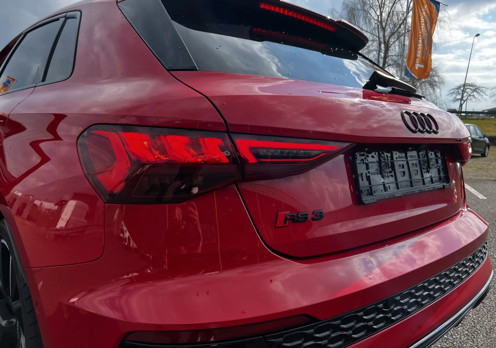 Vue 3/4 arrière droite d'une Audi RS3 Sportback rouge avec feux LED et logo RS3 visible sur le hayon.
