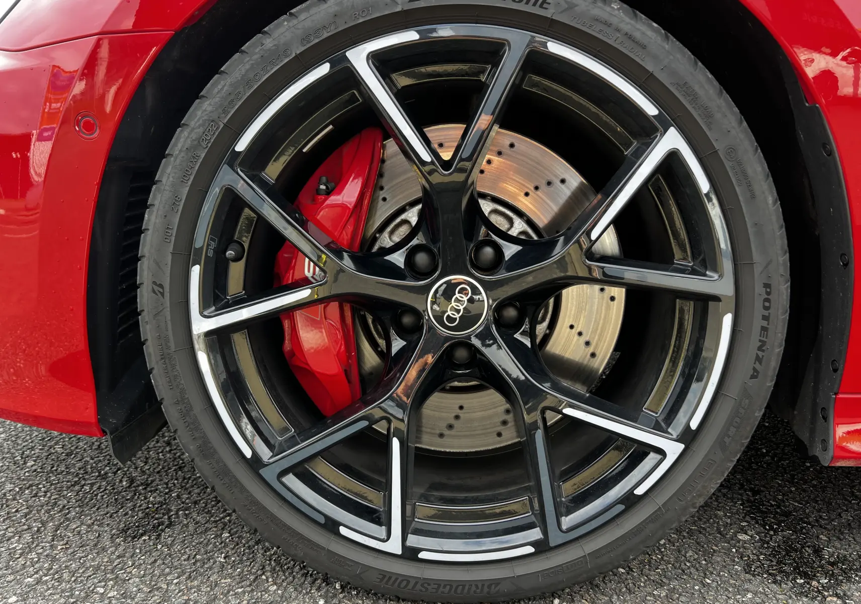 Gros plan sur la roue avant droite noire et argentée de l'Audi RS3 Sportback rouge avec étrier de frein rouge visible.