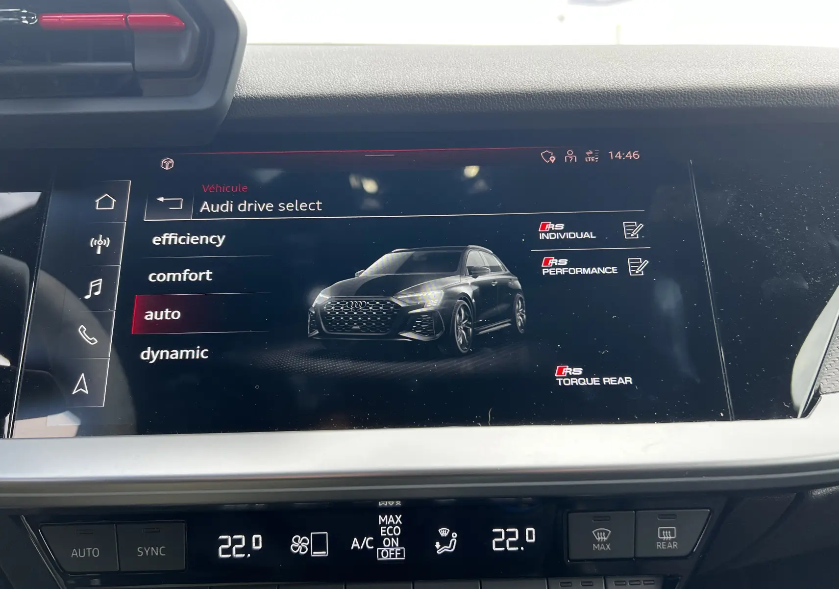 Écran central affichant les modes de conduite d'une Audi RS3 Sportback rouge vue de face en 3/4.