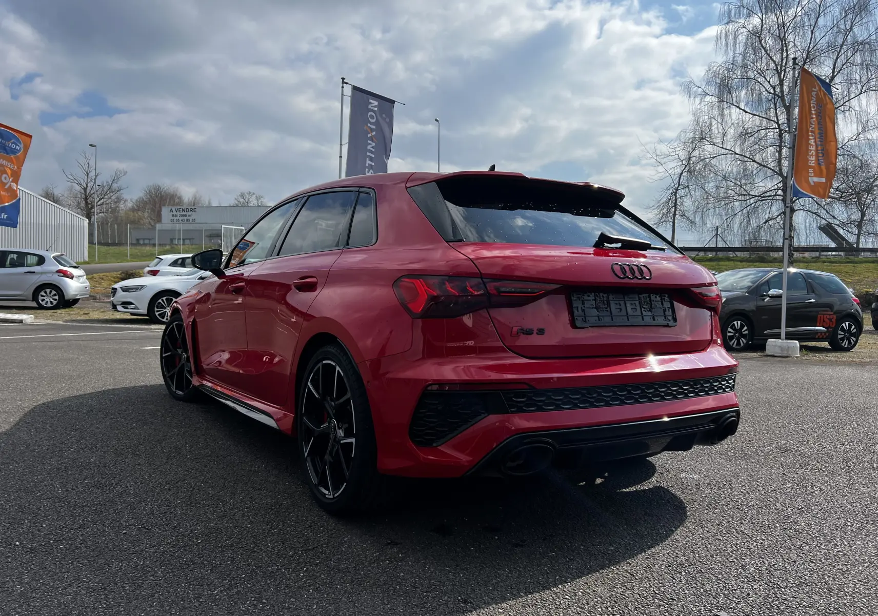 Audi RS3 Sportback rouge vue 3/4 arrière droit, avec jantes noires et double sortie d'échappement sportive.