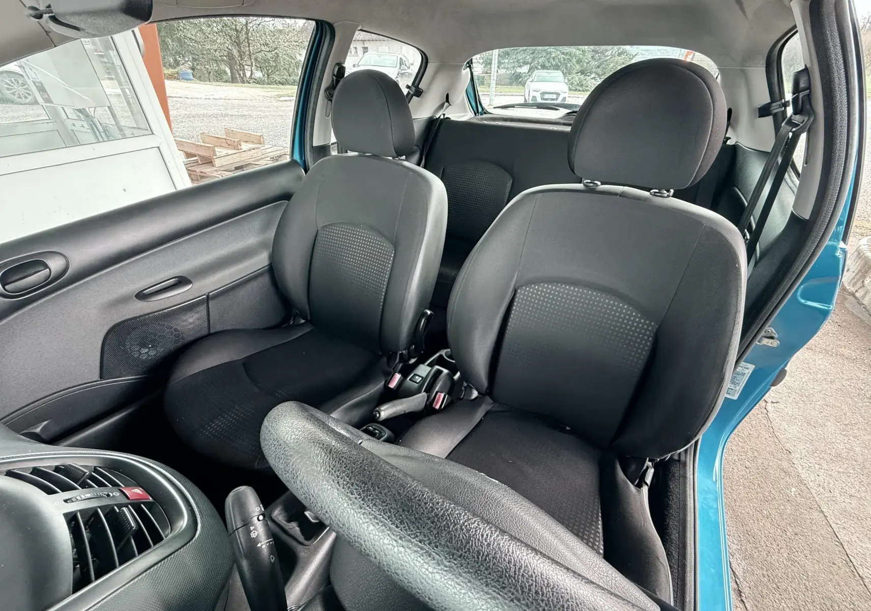 Vue intérieure avant droite de la Peugeot 206+ bleue de 2011, montrant les sièges noirs en tissu et cuir et le volant.