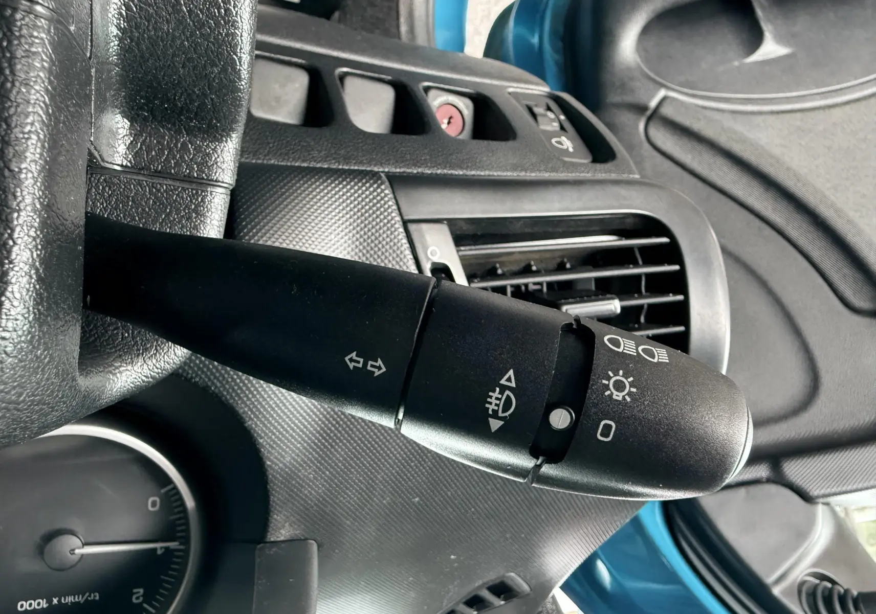 Gros plan sur la commande de clignotants à gauche du volant d'une Peugeot 206+ bleu, intérieur noir.