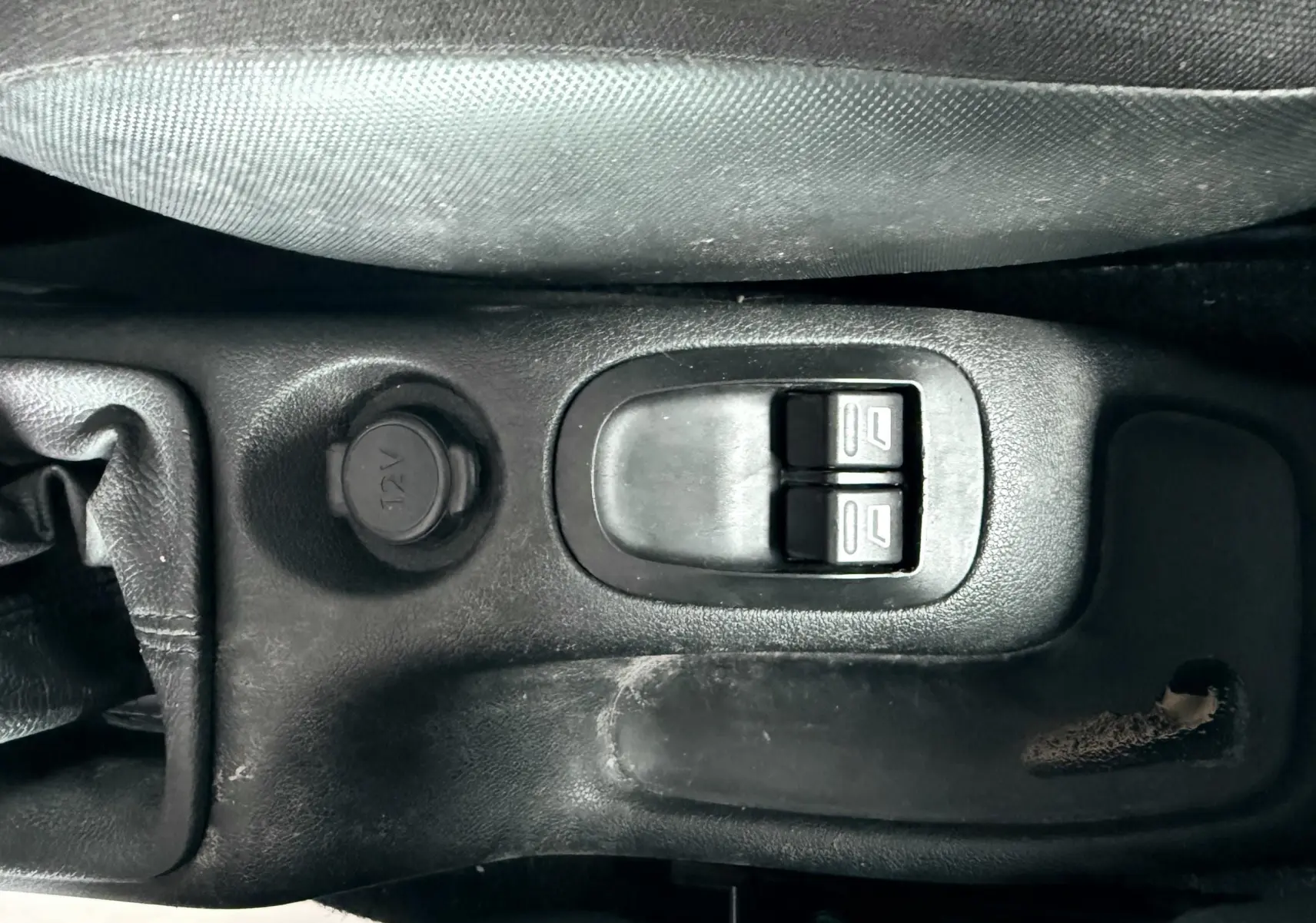 Gros plan sur la console centrale noire de la Peugeot 206+ 2011, montrant les commandes de vitres électriques et prise 12V.