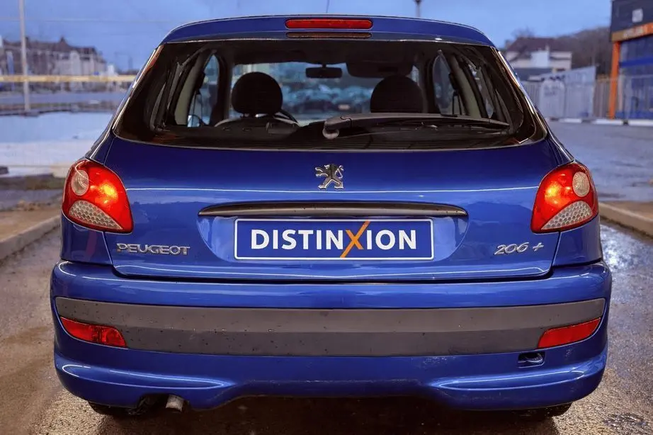 Vue arrière d'une Peugeot 206+ bleue avec feux allumés et plaque d'immatriculation Distinxion.