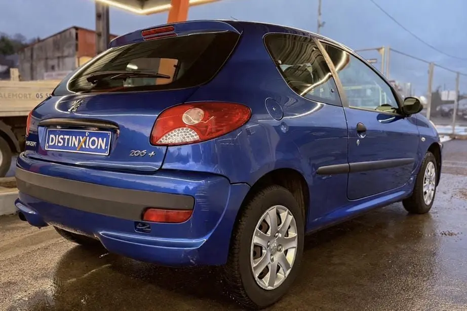 Peugeot 206+ bleu vue 3/4 arrière droit, compacte 3 portes avec feux arrière rouges et jantes alliage.