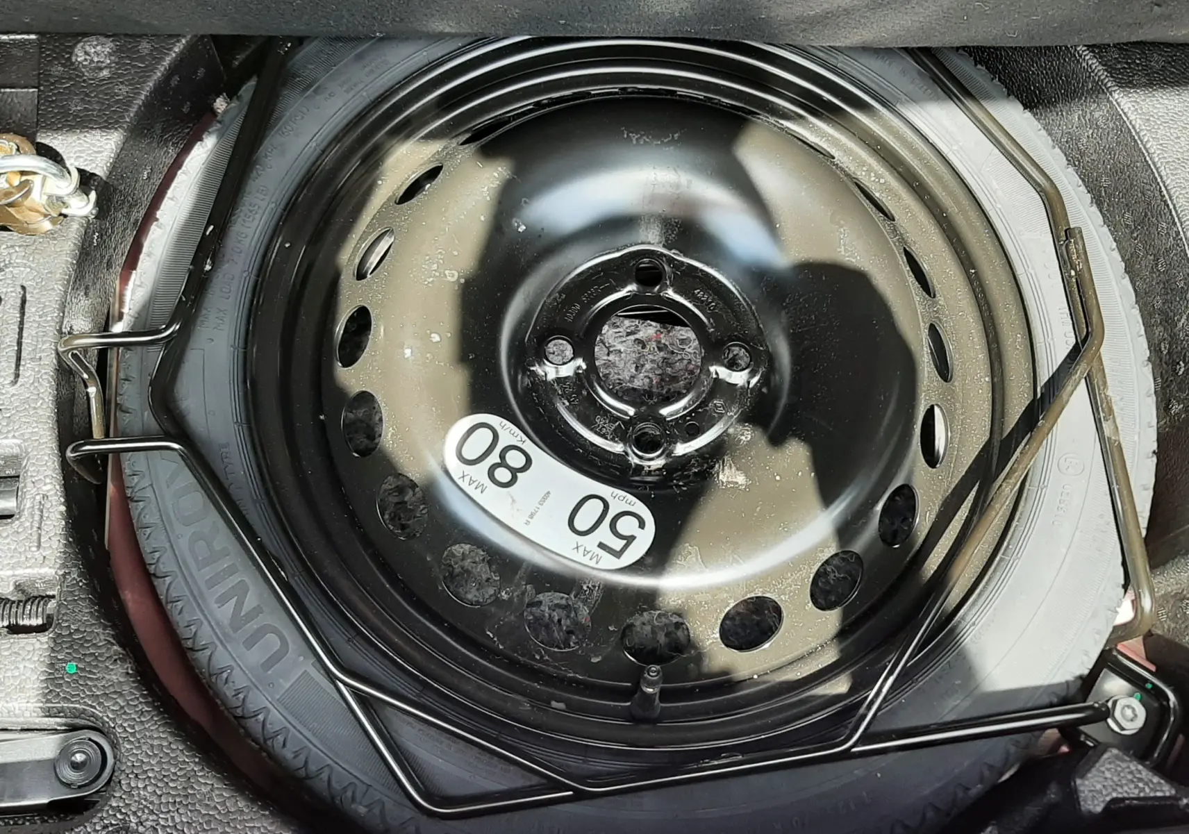 Vue rapprochée de la roue de secours noire dans le coffre de la Renault Clio V rouge flamme 2025.