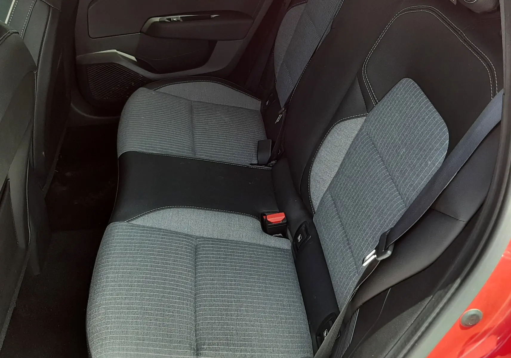 Vue intérieure côté arrière droit de la Renault Clio V rouge flamme, montrant les sièges arrière gris et noirs en tissu et cuir.