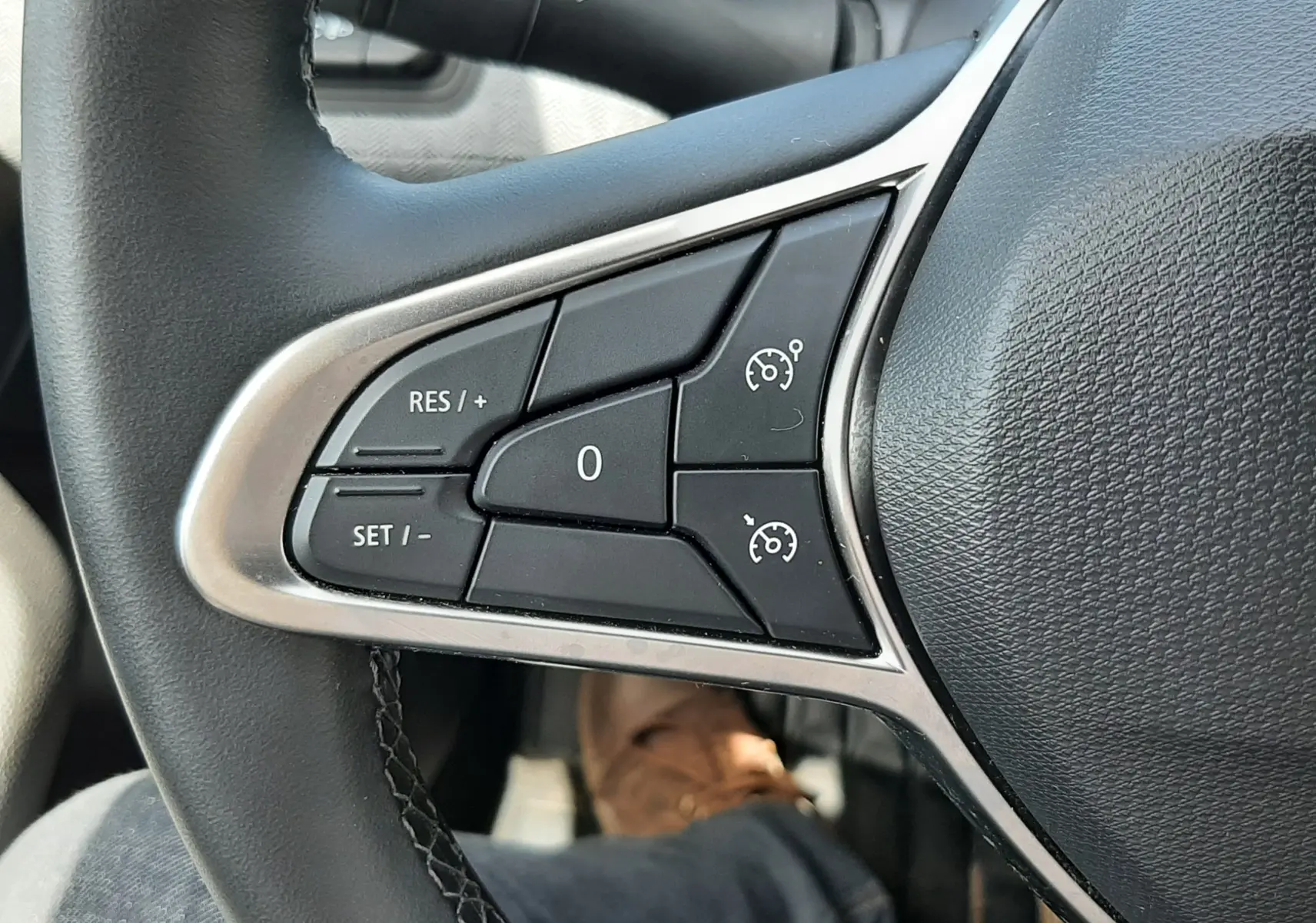 Gros plan sur les commandes au volant côté gauche de la Renault Clio V, finition gris noir, boutons de régulateur de vitesse.