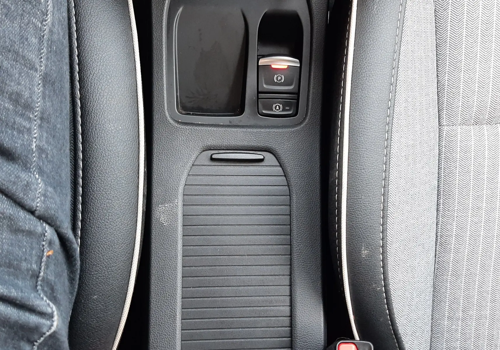 Vue plongeante sur la console centrale noire de la Renault Clio V, avec commandes de frein à main électronique et bouton start/stop.