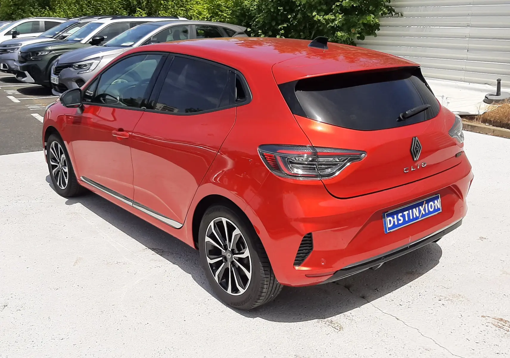 Renault Clio V rouge flamme métal vue 3/4 arrière droit, avec vitres teintées et jantes alliage noires.
