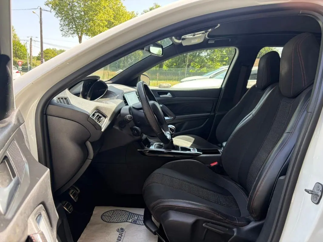 Vue intérieure côté conducteur de la Peugeot 308 GT-Line blanche de 2017, avec sièges noirs et volant multifonction.
