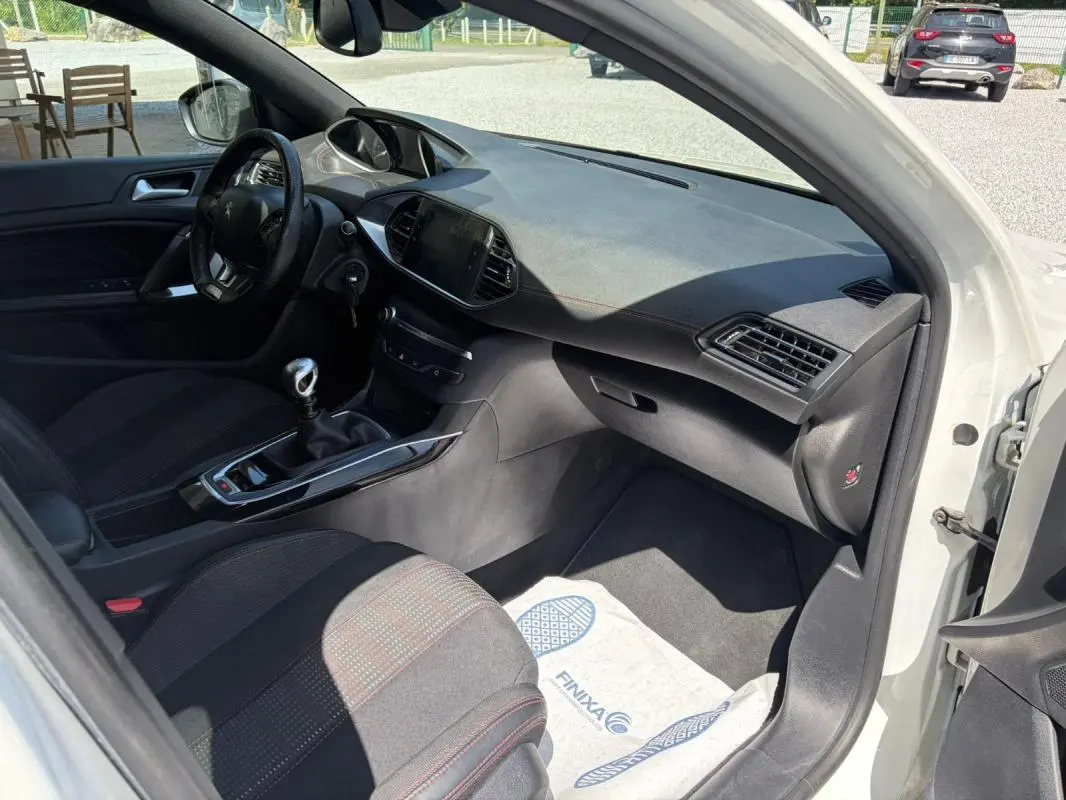 Intérieur de la Peugeot 308 GT-Line 2017 vue côté passager, avec tableau de bord noir et sièges tissu noir à surpiqûres rouges.