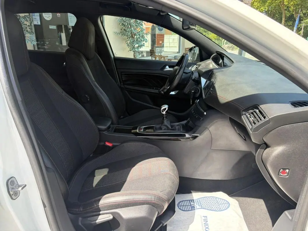 Vue intérieure côté gauche de la Peugeot 308 GT-Line blanche de 2017, avec sièges noirs et levier de vitesse manuel visible.
